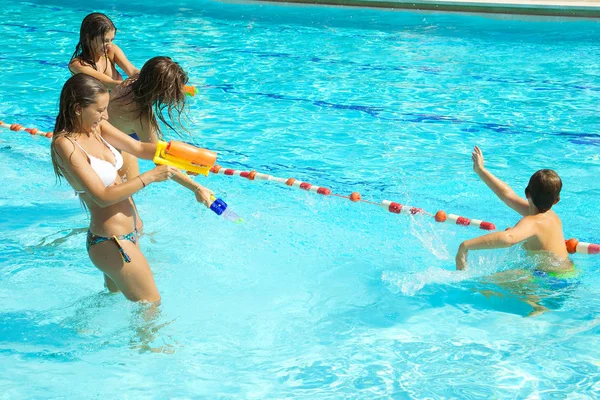 Happy girls playing with kid in pool with water gun — Stock Photo, Image