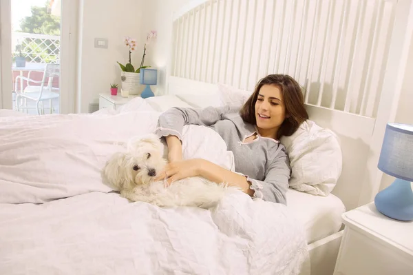 Χαριτωμένο γυναίκα παίζει με το σκύλο στο κρεβάτι στο σπίτι — Φωτογραφία Αρχείου