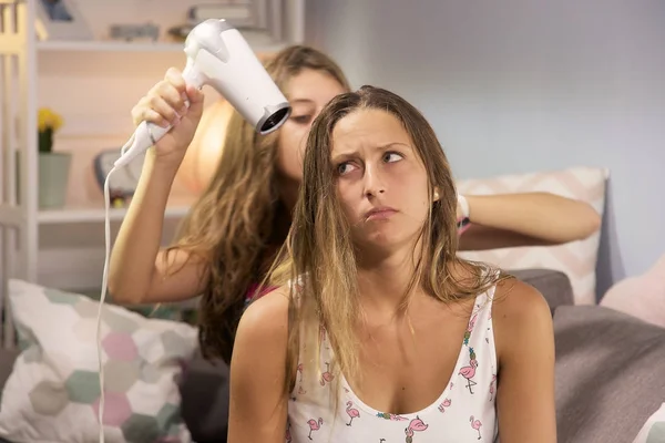 Girl making funny face while girlfriend is drying her long hair — Stock Photo, Image