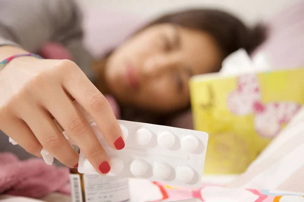Woman in bed taking medicine focus on pills — Stock Photo, Image