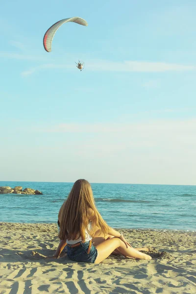 Chica rubia sentada frente al océano mirando pequeño motor de parapente — Foto de Stock