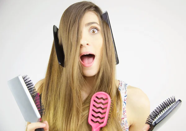 Woman making funny expression with combs and brushes in her long hair — Stock Photo, Image