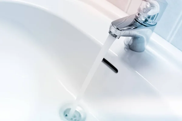 Eau coulant d'un robinet dans un évier blanc — Photo