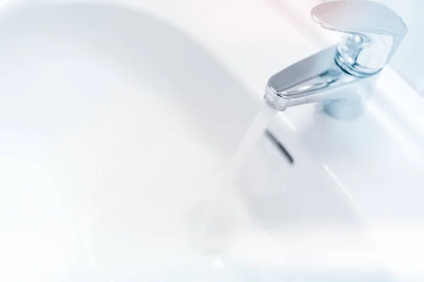 Eau coulant d'un robinet dans un évier blanc — Photo