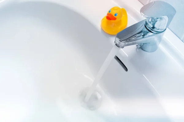 Eau coulant d'un robinet dans un évier blanc avec un canard en caoutchouc — Photo