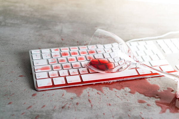 Красное вино пролилось на клавиатуру компьютера на бетонный стол
