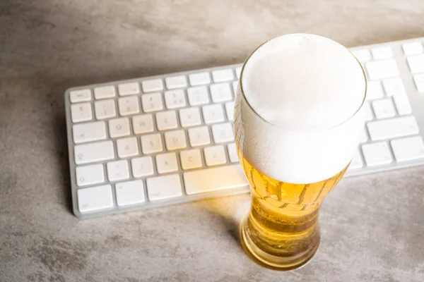 Cerveja ao lado do teclado do computador na mesa de concreto — Fotografia de Stock