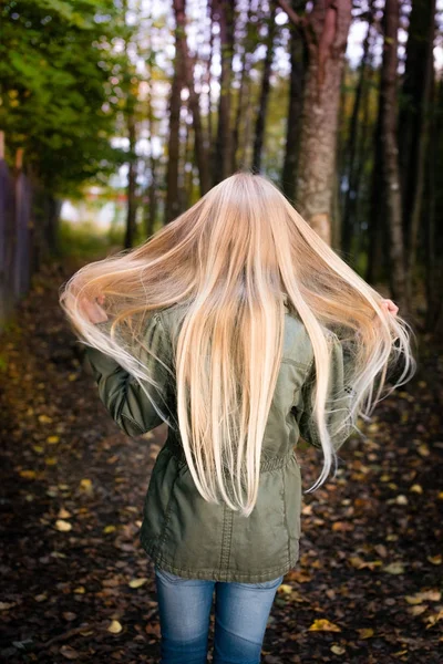 Girl from behind outside waiving her long blonde hair