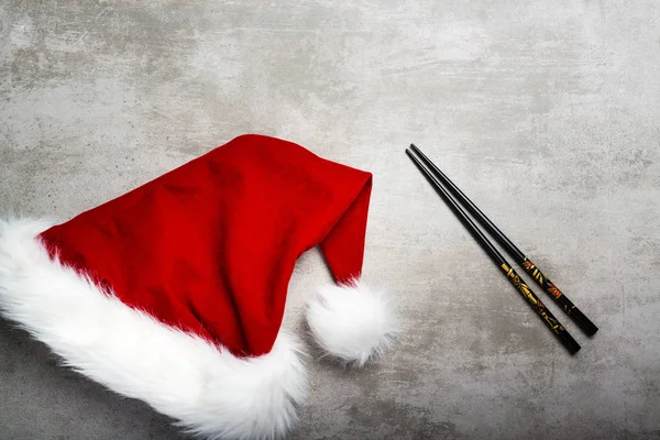 Red santa hat and chopsticks on a gray concrete table — Stock Photo, Image