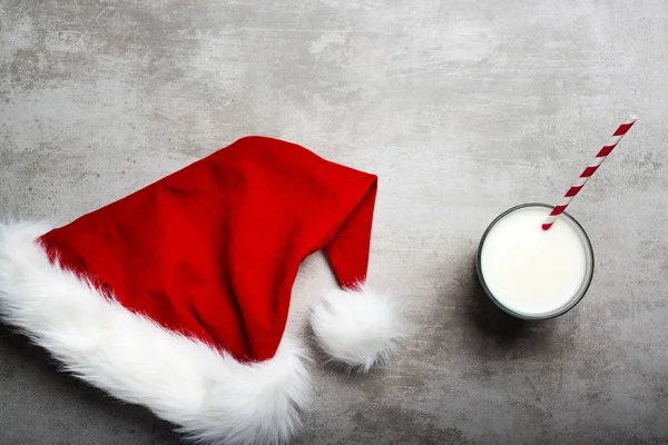 Red santa hat and a glass of milk on a gray concrete table — Stock Photo, Image