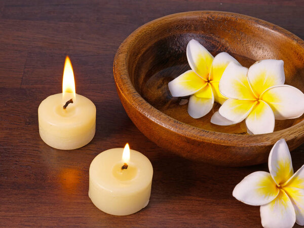 two candles and a bowl of water with white tropical flowers