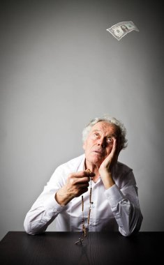 Yaşlı adam ile tespih dua ediyor. Düşen bir dolar.