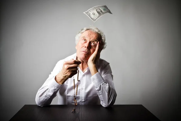 Oude man is bidden met rozenkrans kralen. Dalende één dollar. — Stockfoto