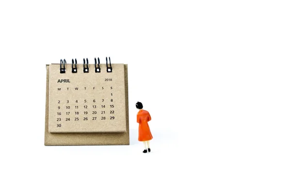 April. Calendar sheet and miniature plastic woman on white backg — Stock Photo, Image