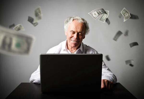 Stary człowiek przy użyciu laptopa. Stary człowiek w białym zarabia dolarów na w — Zdjęcie stockowe