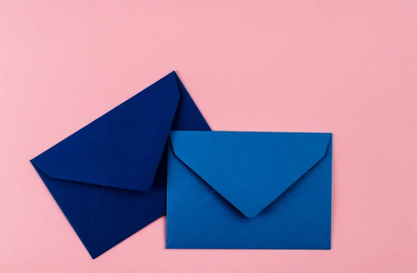 粉色背景上的蓝色信封 桌上的邮包 免版税图库图片