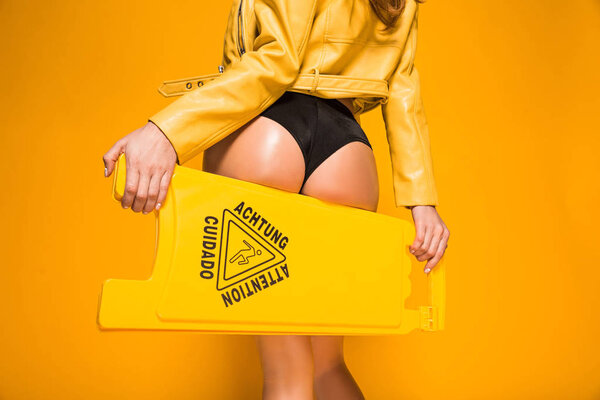 cropped image of sexy woman holding wet floor sign on orange
