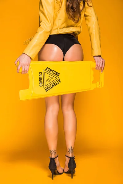 cropped image of seductive woman holding wet floor sign on orange