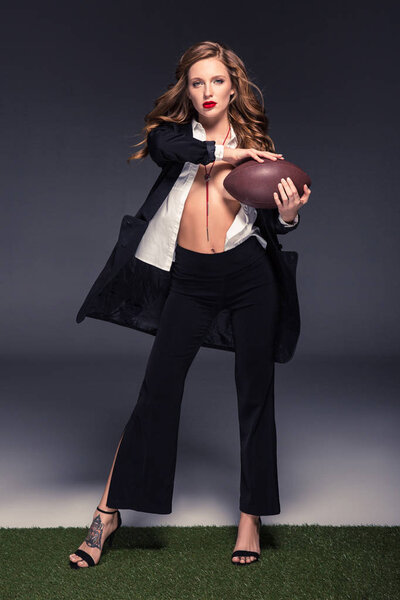 seductive woman in unbuttoned shirt and jacket holding american football ball
