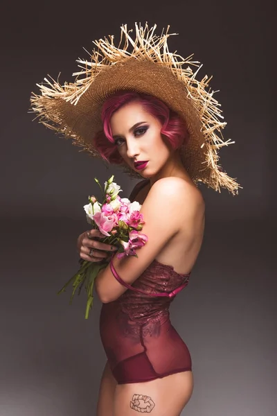 きれいなピンクの花灰色の背景の前でポーズをとって麦藁帽子で髪の巻き毛の少女 ストック写真