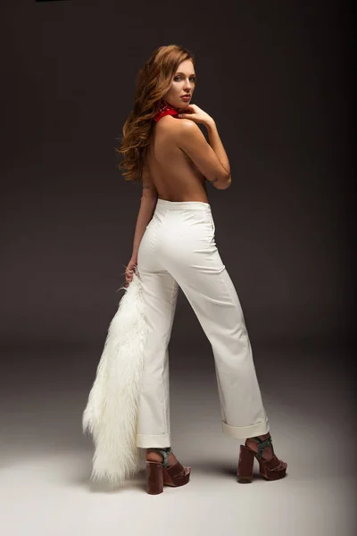 Mujer sexy con la espalda desnuda en pantalones blancos mirando por encima del hombro - foto de stock