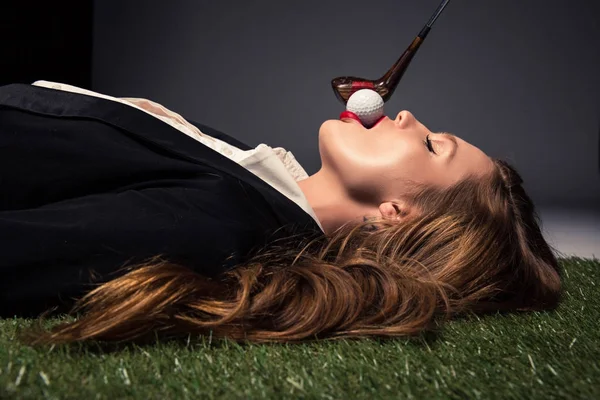 Vue latérale de la femme séduisante couchée sur l'herbe avec balle de golf dans la bouche — Photo de stock