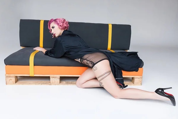 Красива татуйована дівчина в прозорій білизні позує на дивані — стокове фото