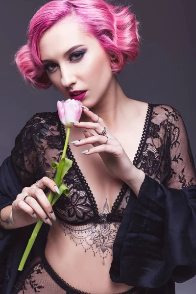 Séduisante fille tatouée en lingerie transparente avec fleur devant fond gris — Photo de stock