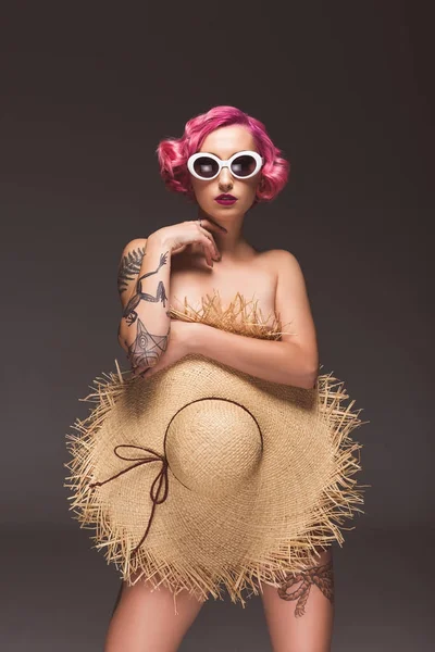 Hermosa chica desnuda pin up en gafas de sol que cubre con sombrero de paja en frente de fondo gris — Stock Photo