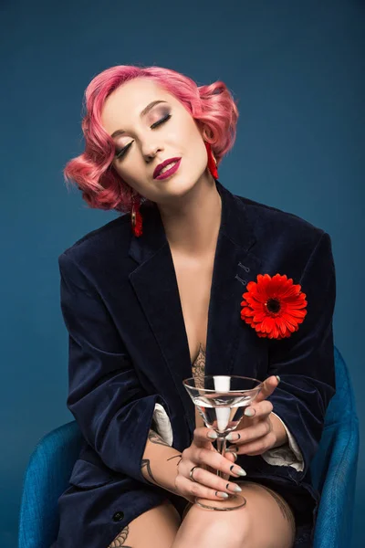 Beautiful tattoed pin up girl in jacket with boutonniere and wineglass infront of blue background — Stock Photo