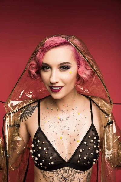 Beautiful pink haired girl with tattoos in lingerie and raincoat infront of red background — Stock Photo