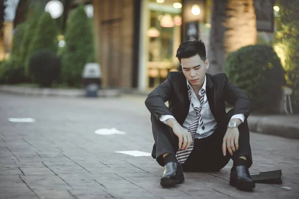 Tired or stressed businessman sitting on the walkway in the city