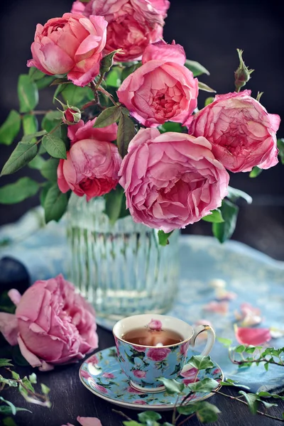 Delicate beautiful pink roses from a garden in a glass vase. English Roses,Variety - Princess Alexandra of Kent. And a tea in a beautiful porcelain cup.