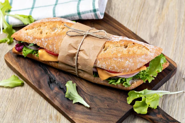 fresh submarine sandwich with ham, cheese, bacon, tomatoes, lettuce, on wooden cutting board