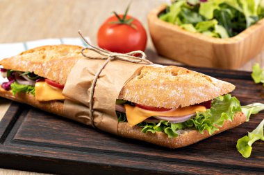 fresh submarine sandwich with ham, cheese, bacon, tomatoes, lettuce, on wooden cutting board clipart