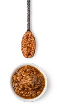 Beyaz arka planda kırmızı pesto soslu kase ve kaşık.