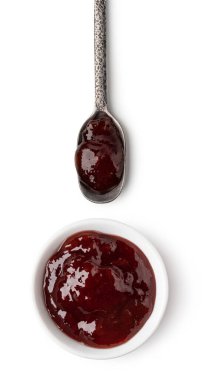 Beyaz arka planda küçük cam kase ve bir kaşık kırmızı böğürtlen reçeli.