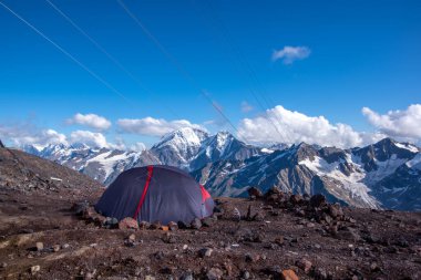 Keşif çadırını kapatın, kayalarla korunuyor. Elbrus Dağı, Kafkasya, Rusya. Dağlarda konaklama yeri. Arka tarafta gökyüzü ve beyaz bulutlar. Arka Görünüm.