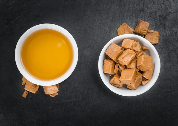 Caramel syrup and candies in bowls — Stock Photo, Image