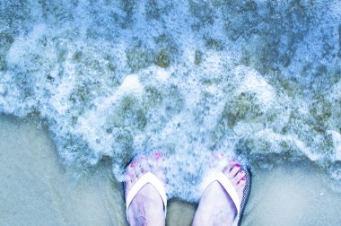 Sahilde sandalet giyen kadın resmi.