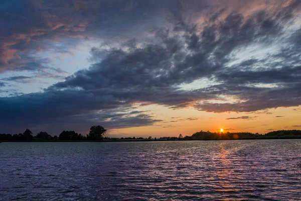 Nubes oscuras en el cielo sobre el lago y la puesta de sol — Foto de Stock