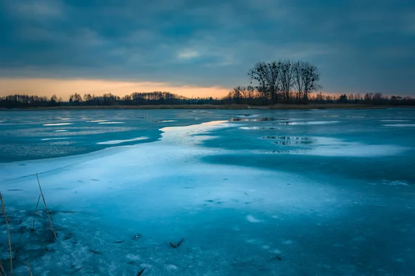 Gelo em um lago congelado, árvores no horizonte e o céu da noite após o pôr do sol — Fotografia de Stock