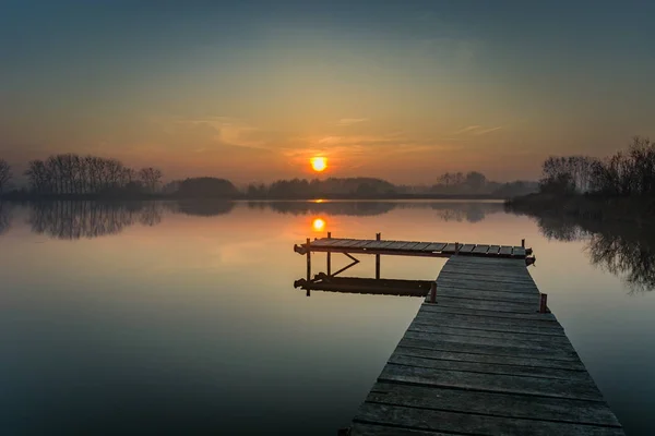 Dřevěné molo na klidném jezeře, večerní obloze a západu slunce — Stock fotografie