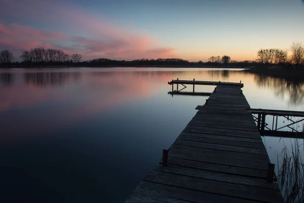 Houten steiger op een rustig meer en roze wolken na zonsondergang — Stockfoto