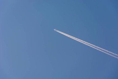 Yüksekten uçan tüylü bir yolcu uçağı ve gökyüzünde beyaz çizgiler.