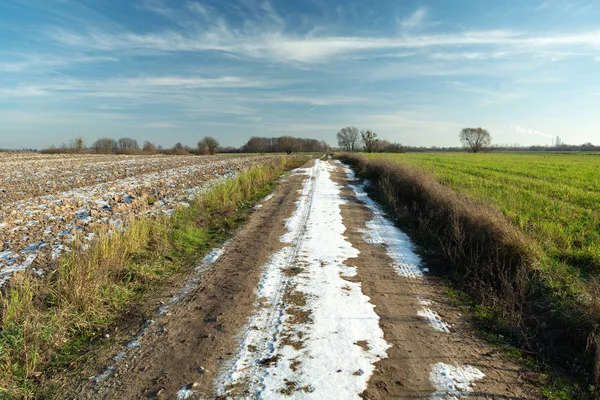 Primera nieve en un camino de tierra a través de campos y nubes en el cielo —  Fotos de Stock