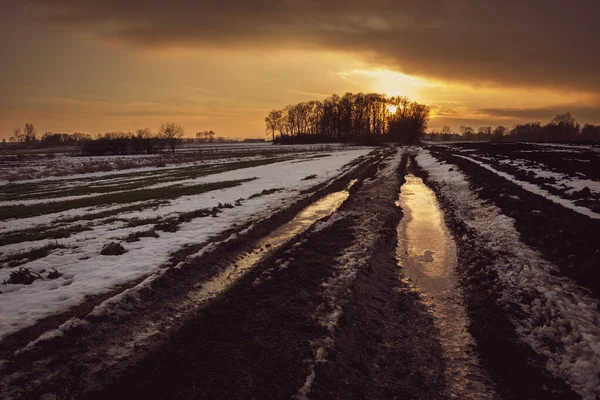 Modderige bevroren landelijke weg door velden, wolken en zonsondergang, uitzicht in de winter avond — Stockfoto