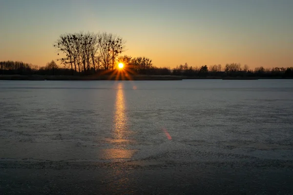 A frozen lake, trees on the horizon and the glow of the setting sun, evening view — Stock Photo, Image