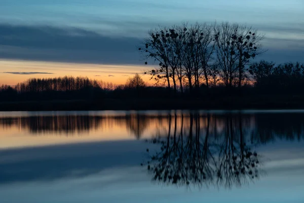 Árvores na margem do lago, imagem espelhada de nuvens noturnas na água no leste da Polônia — Fotografia de Stock