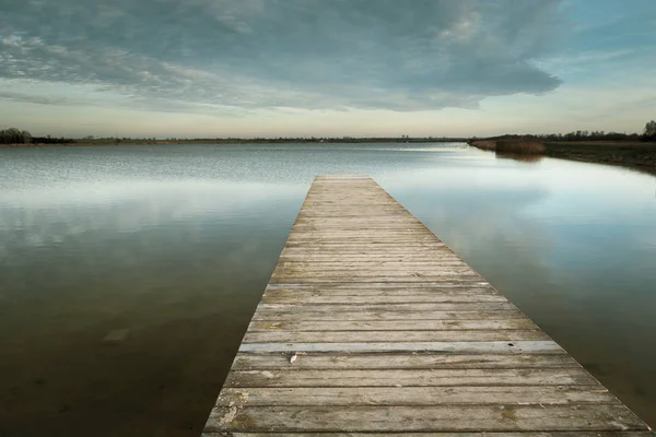 Lange houten brug op het kalme meer, avondwolken aan de hemel — Stockfoto